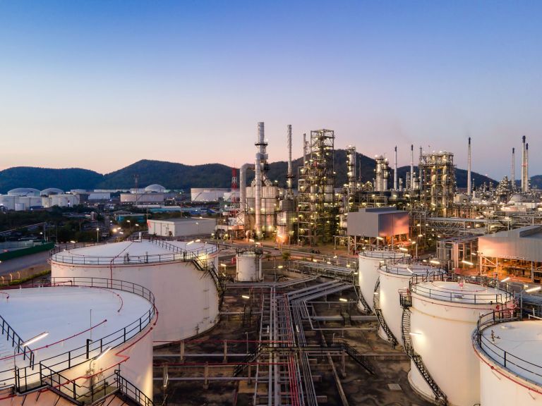Beautiful sunset view of an oil refinery with illuminated structures and surrounding mountains at dusk.