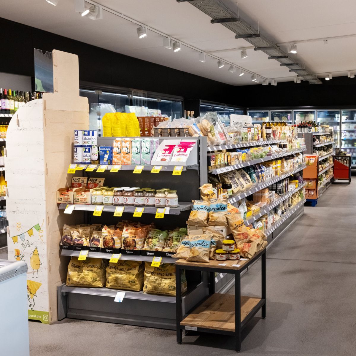 A modern, well-organized grocery aisle featuring shelves stocked with various vegan and organic food products in a clean, retail environment.