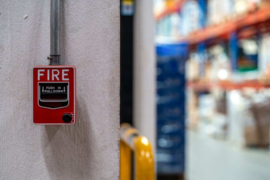 Red fire alarm switch on the concrete wall in the office building. Industrial fire warning system equipment for emergency.