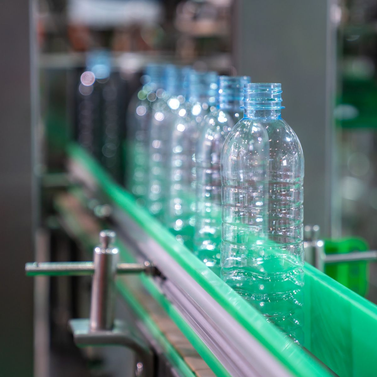 Empty plastic bottles move along a green industrial conveyor belt in an automated beverage bottling facility.