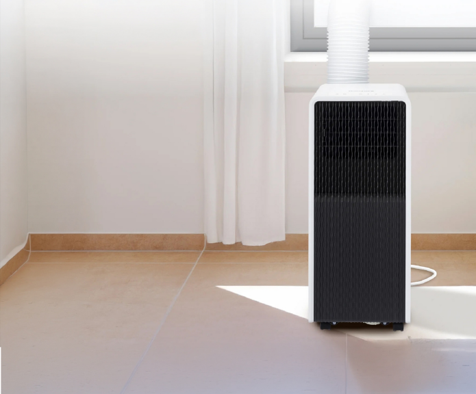 Honeywell portable air conditioner positioned near a window with an exhaust hose, black wave-pattern front grille and white housing.