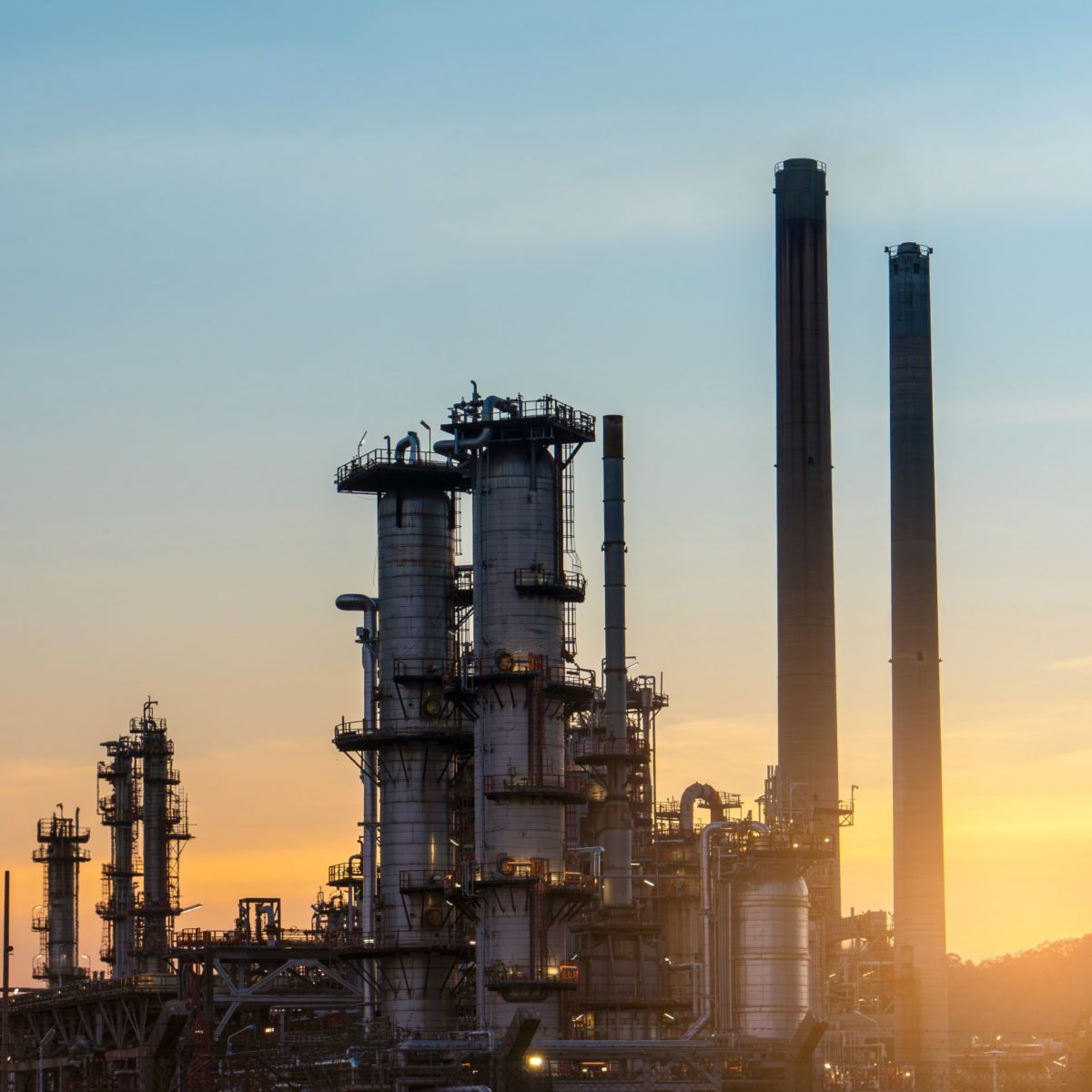  A silhouetted image of an industrial facility at sunset, featuring multiple towers and smoke stacks.