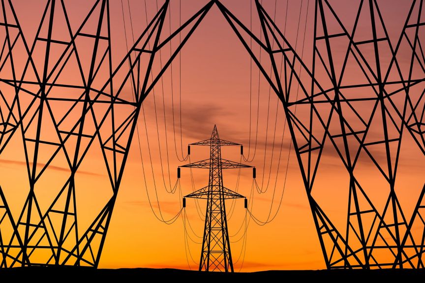 Silhouetted high-voltage electricity pylons frame a central tower against a vibrant orange sunset sky.