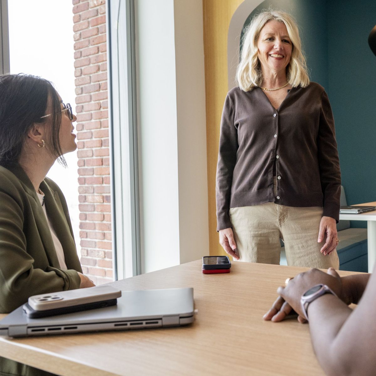 A diverse group of professional women gather around a modern office table for a collaborative team meeting in a well-lit workspace.