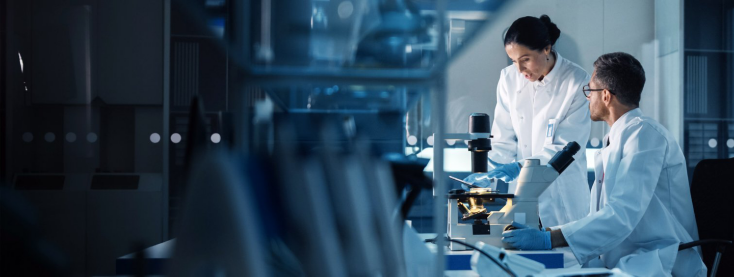 Two laboratory researchers collaborate beside a microscope in a dark, modern lab.
