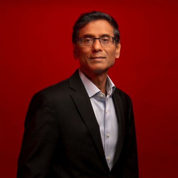 Professional portrait of  Sabi Varma, captured against a bold red background.
