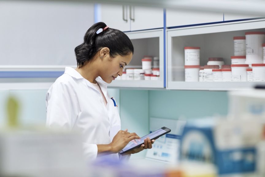 A focused scientist in a lab coat uses a digital tablet while working in a clean, organized laboratory environment filled with supplies.