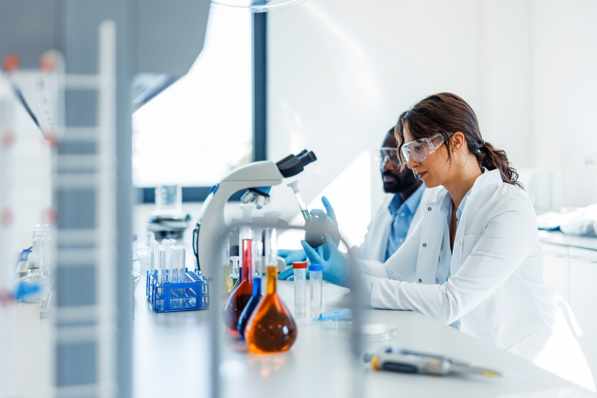 Diverse research team conducts diagnostic experiments using laboratory glassware and microscopy in a bright, modern corporate facility.