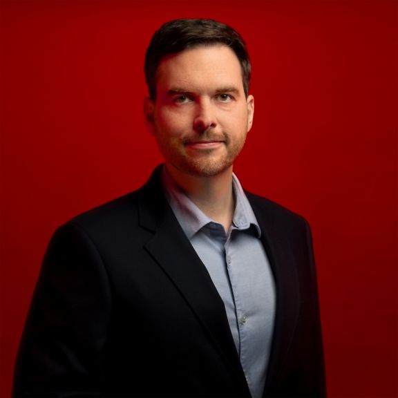 Professional portrait of Scott Hillpott, captured against a bold red background.