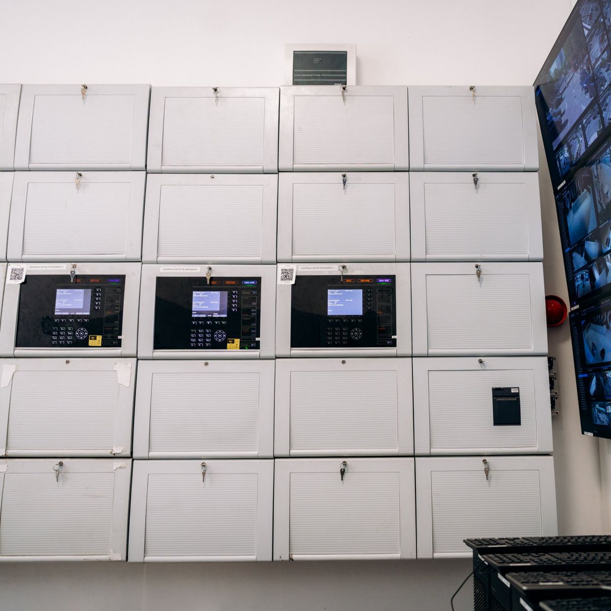 Monitoring station with wall-mounted fire alarm panels and multiple CCTV screens.