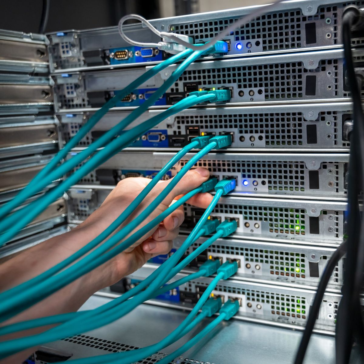 A technician connects a teal ethernet cable into a high-density server rack within a data center environment.