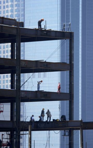 Workers assemble the steel framework of a high-rise building against the backdrop of an urban skyline.