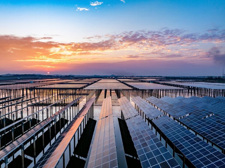 A vast array of floating solar panels stretches across a calm reservoir at sunset, showcasing large-scale renewable energy infrastructure.