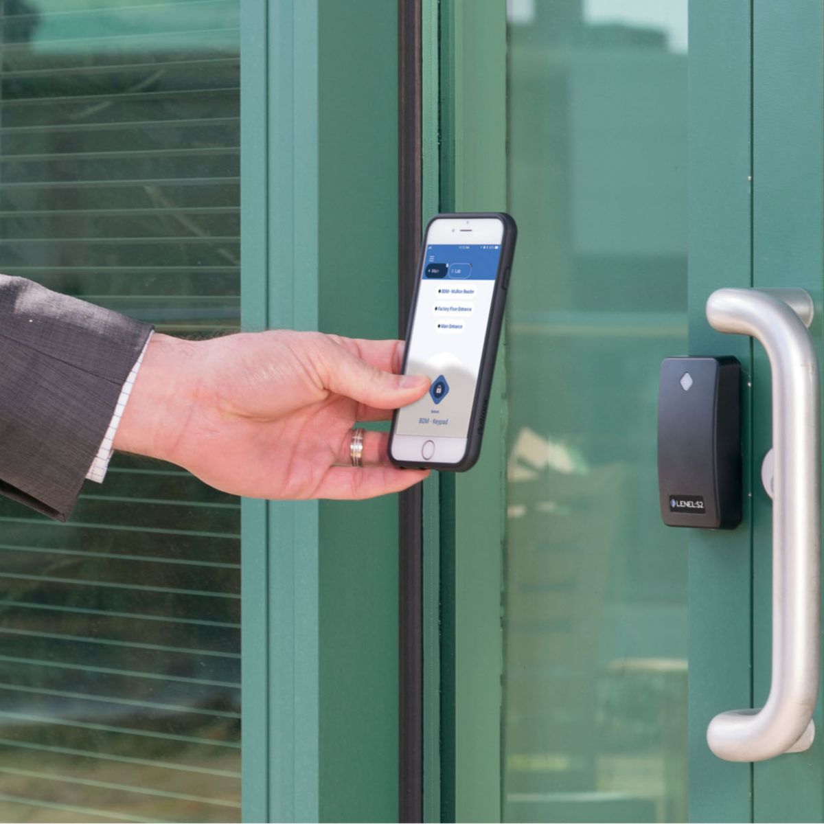 Close-up of a person using a smartphone as a mobile credential at a wall-mounted access reader beside a glass entry door, enabling secure building access.