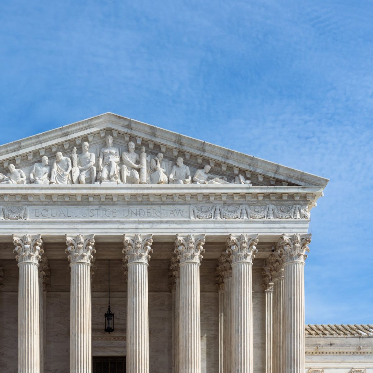A detailed view of the US Supreme Court building facade highlighting the sculpted pediment and iconic Equal Justice Under Law inscription against a blue sky.