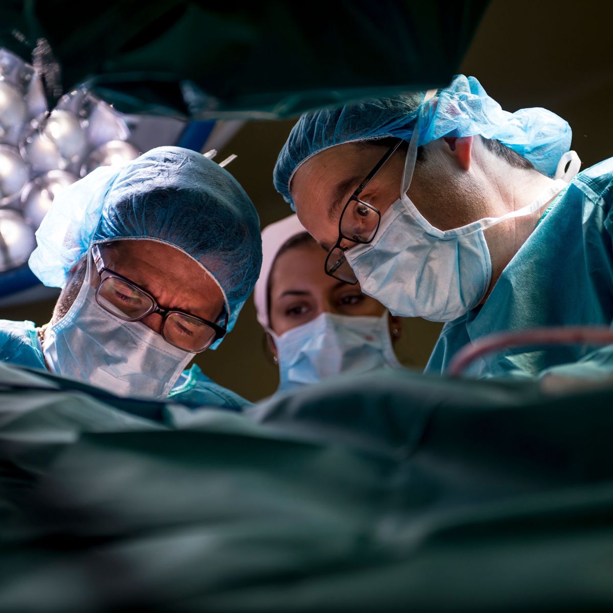 Close-up of medical staff wearing masks and gloves performing a procedure under overhead surgical lights.