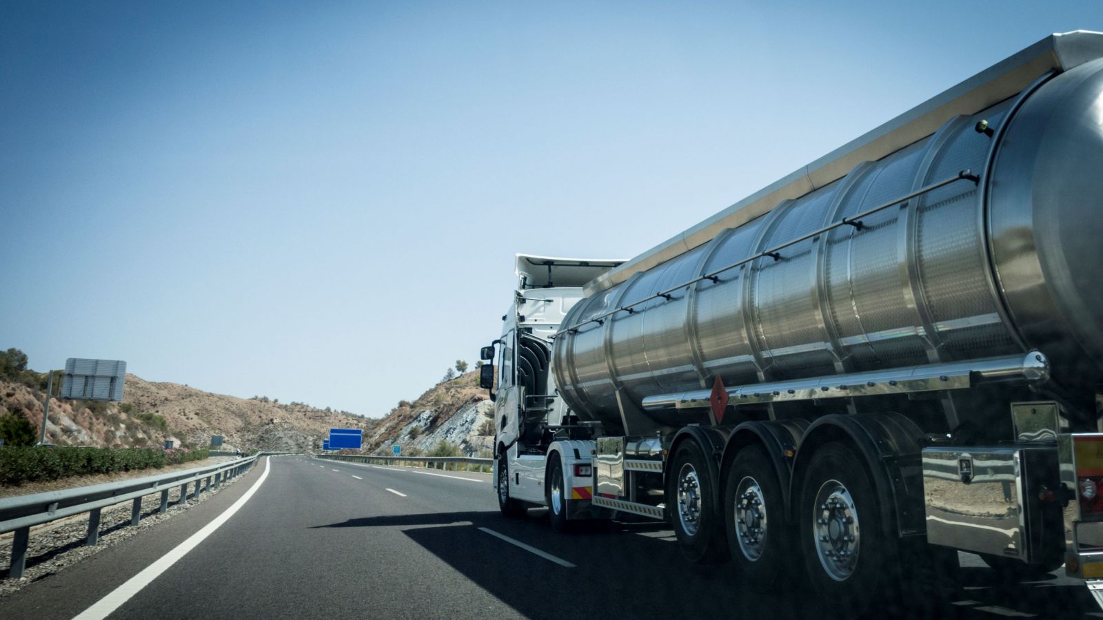 A large tanker truck travels on a highway, transporting liquids through scenic landscapes.