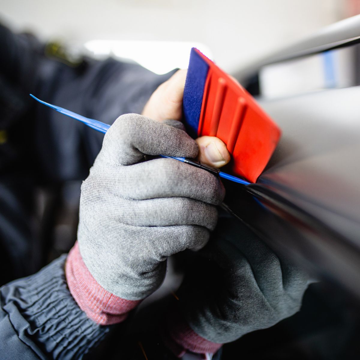 Car wrapping specialist putting vinyl foil or film on car. Selective focus.