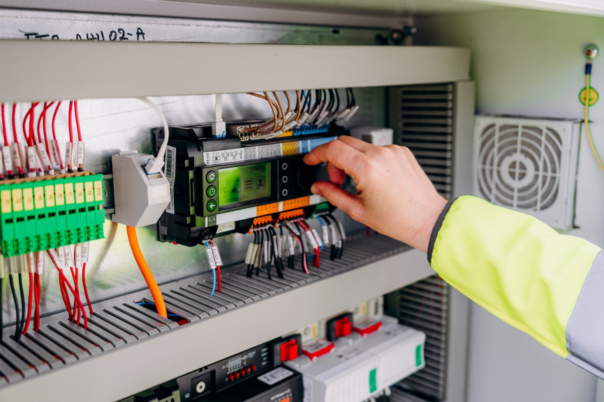 A technician in high-visibility workwear interacts with a digital control module inside a complex electrical junction box.