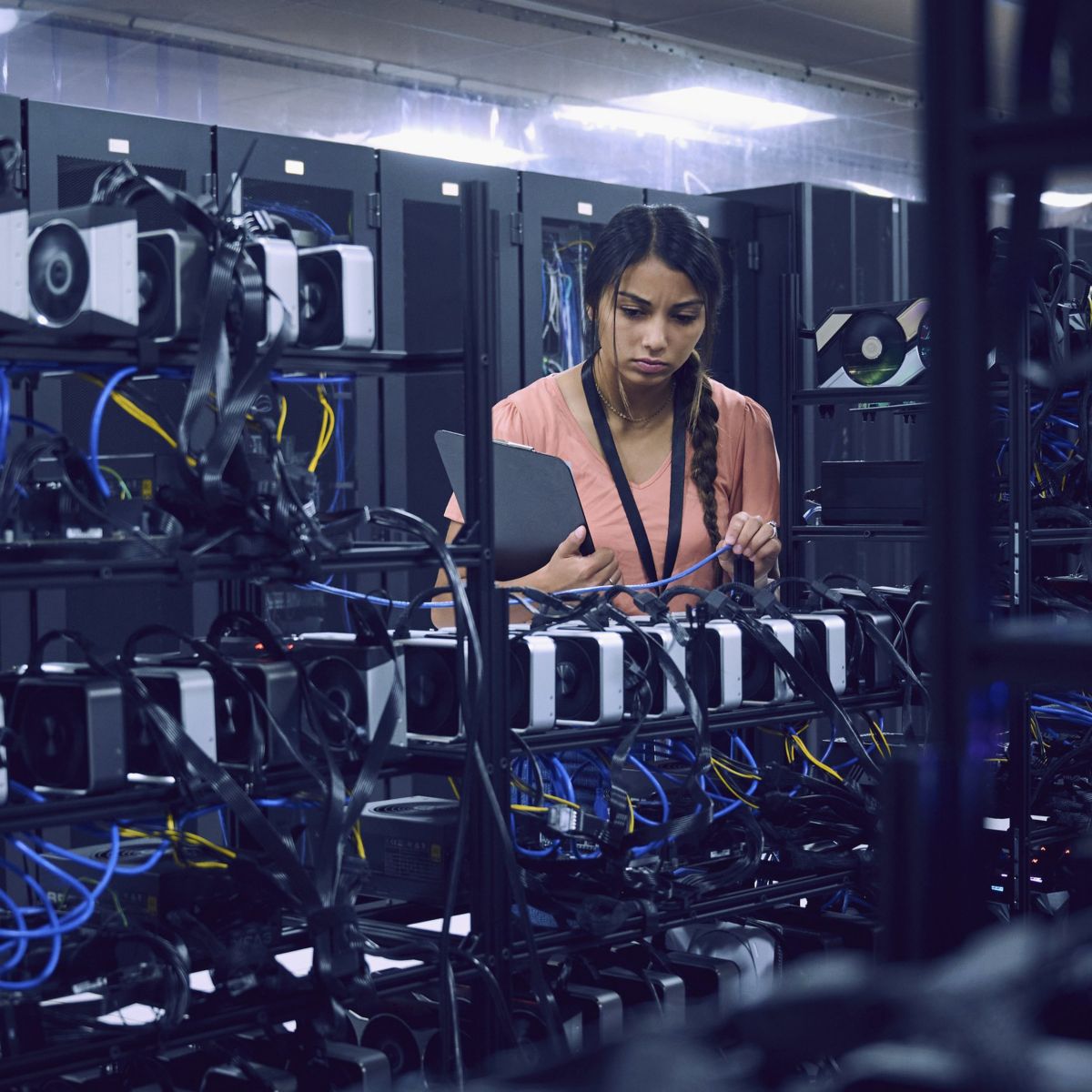 A focused technician inspects cable connections on high-performance server racks within a modern data center facility.