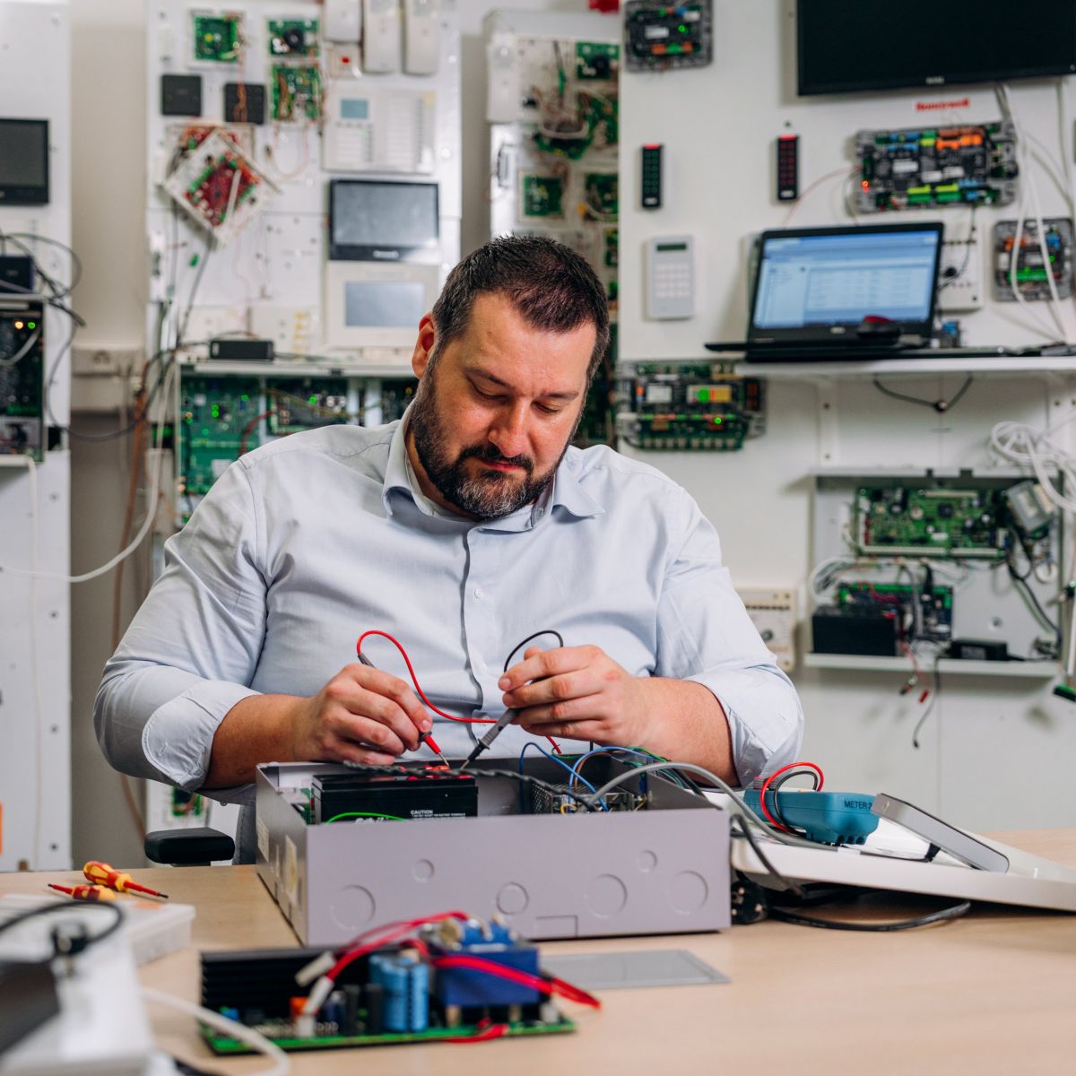 A focused professional uses a multimeter to test circuitry on an open control panel in a technical laboratory environment.