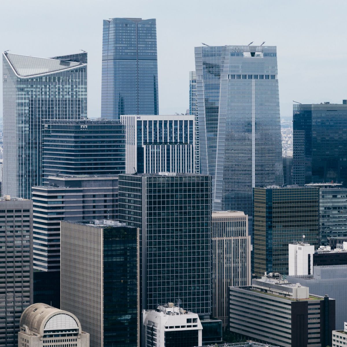 A high-angle view of a dense Tokyo urban district featuring a mix of modern glass skyscrapers, office towers, and active construction sites.