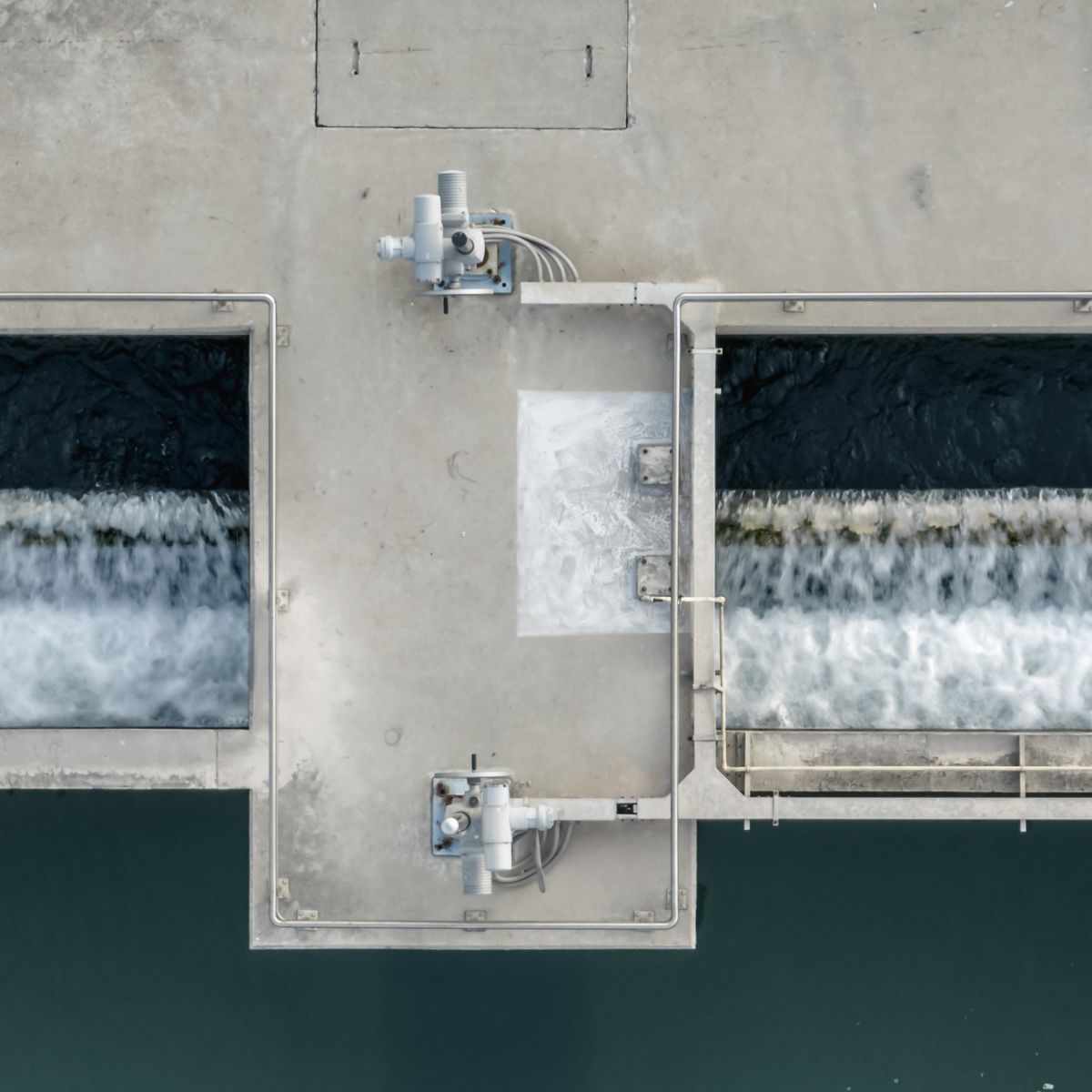 An overhead view captures water cascading over weirs in a symmetrical industrial wastewater treatment plant setting.