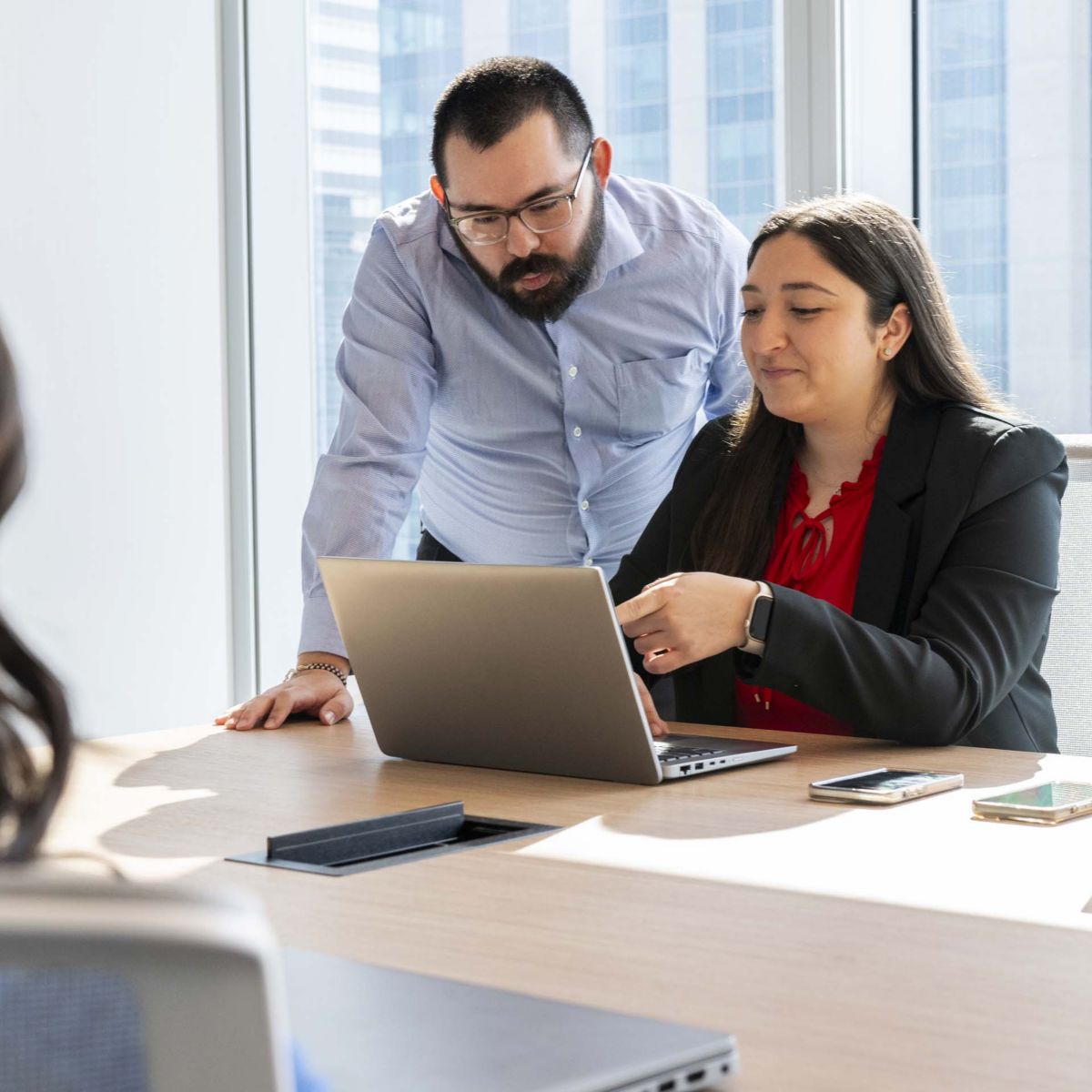 Colleagues working together on a laptop in a professional office environment, representing mentorship, knowledge sharing, and teamwork.