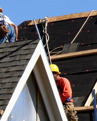 Construction workers putting shingles on the roof of a house. 