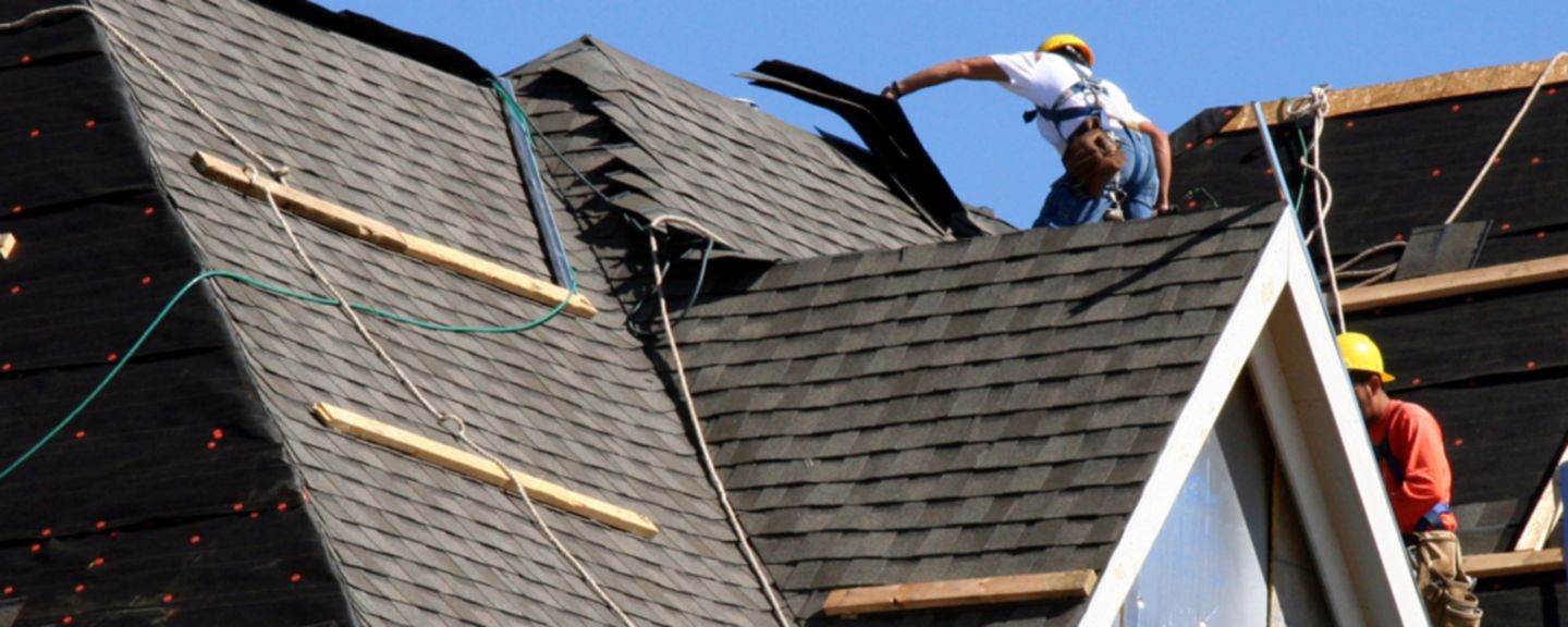 Construction workers putting shingles on the roof of a house. 
