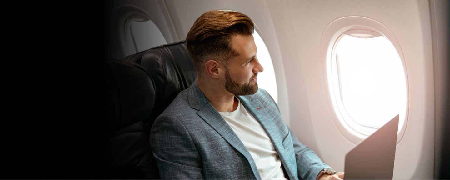 Business traveler seated by an airplane window with a laptop, representing professional mobility and opportunity.