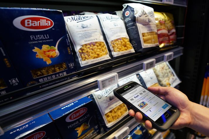 hand using a Honeywell mobile device in front of a shelf
