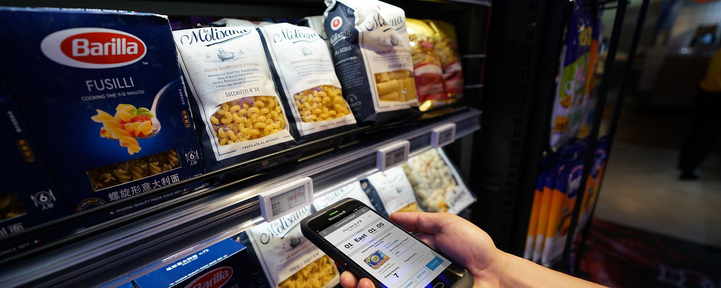 hand using a Honeywell mobile device in front of a shelf