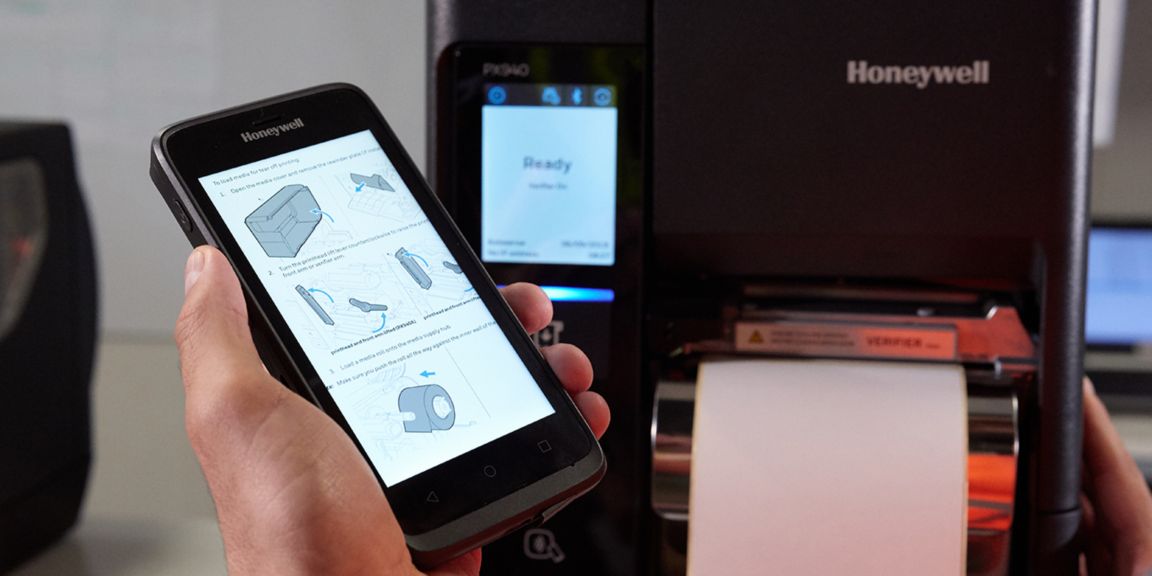 hand holding a Honeywell device in front of a Honeywell printer