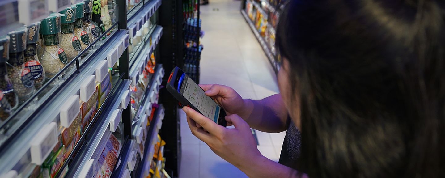 people using a mobile device in front of a shelf with groceries