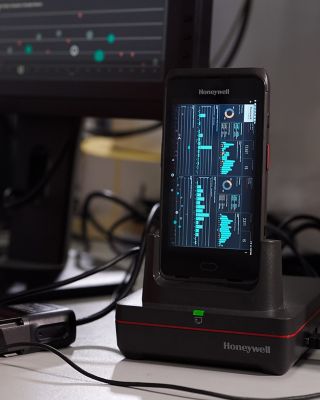 hand on a mouse next to a keyboard and a honeywell device