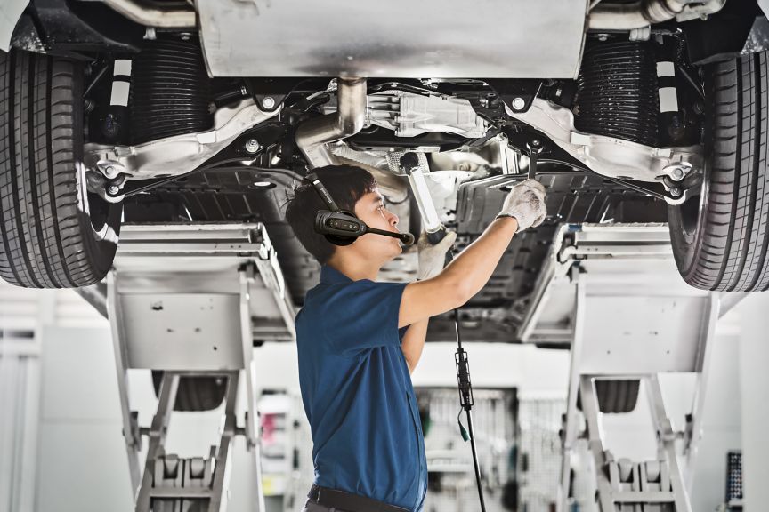 Asian mechanic repairing and light up under the car in maintainance service center which is a part of showroom, technician or engineer professional work for customer, car repair and maintain concet