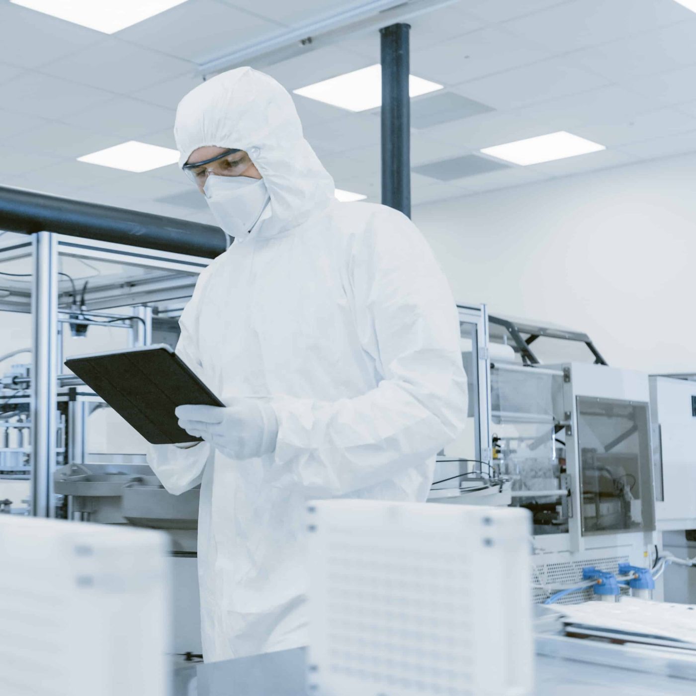 Quality Control Check: Scientist Using Digital Tablet Computer and wearing Protective Suit walks through Manufacturing Laboratory. Product Manufacturing: Pharmaceutics, Semiconductors, Biotechnology.