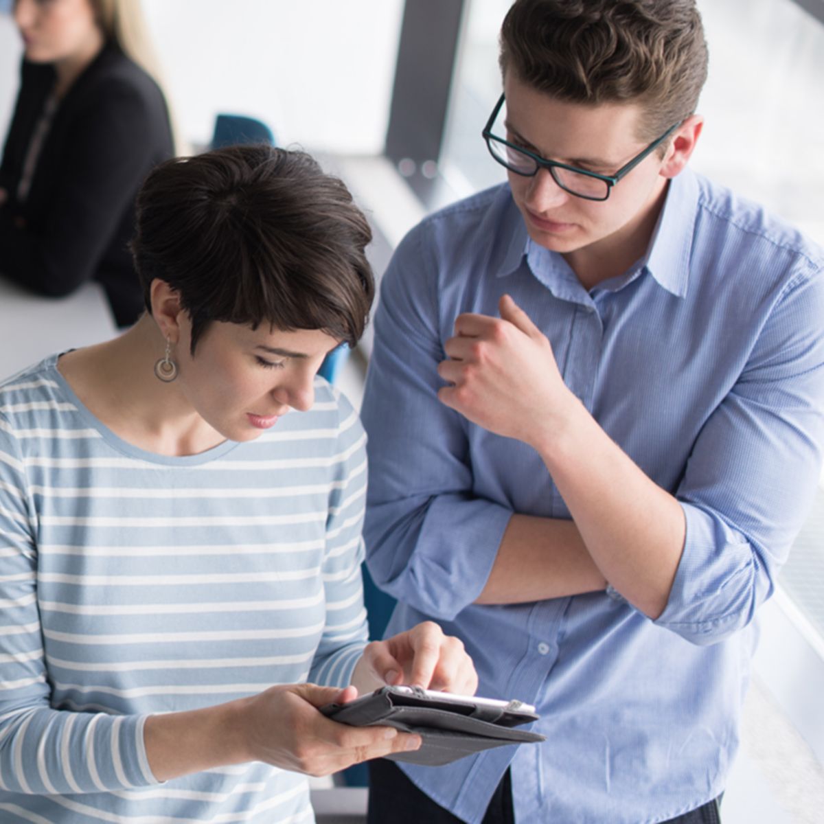two business people using tablet  preparing for next meeting and discussing ideas with colleagues in the background