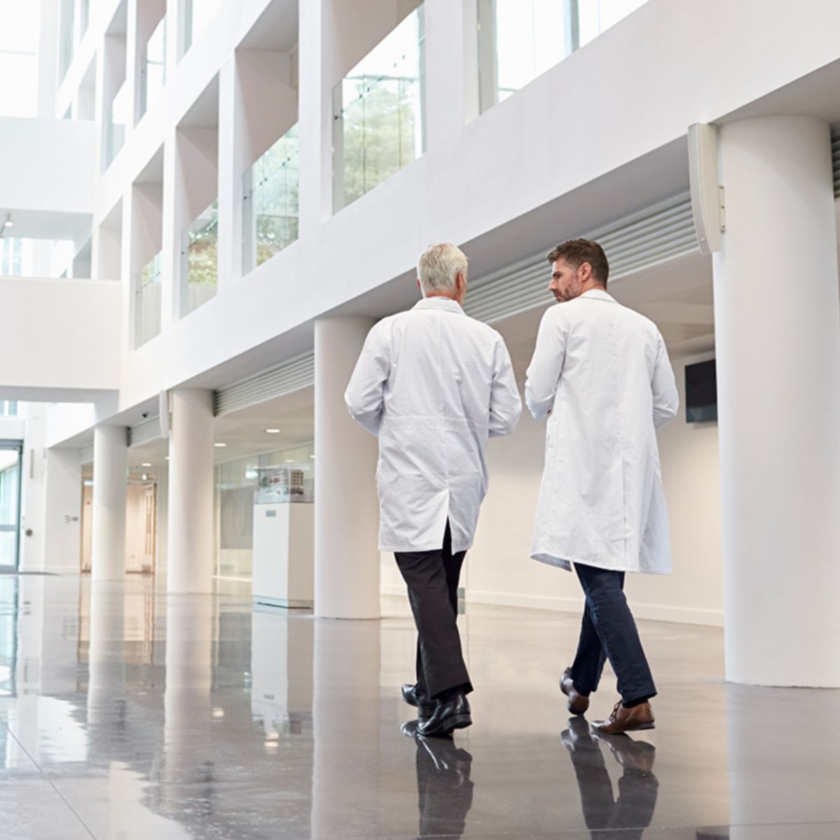 Coworkers walking and using bicycle on office's lobby - with face mask