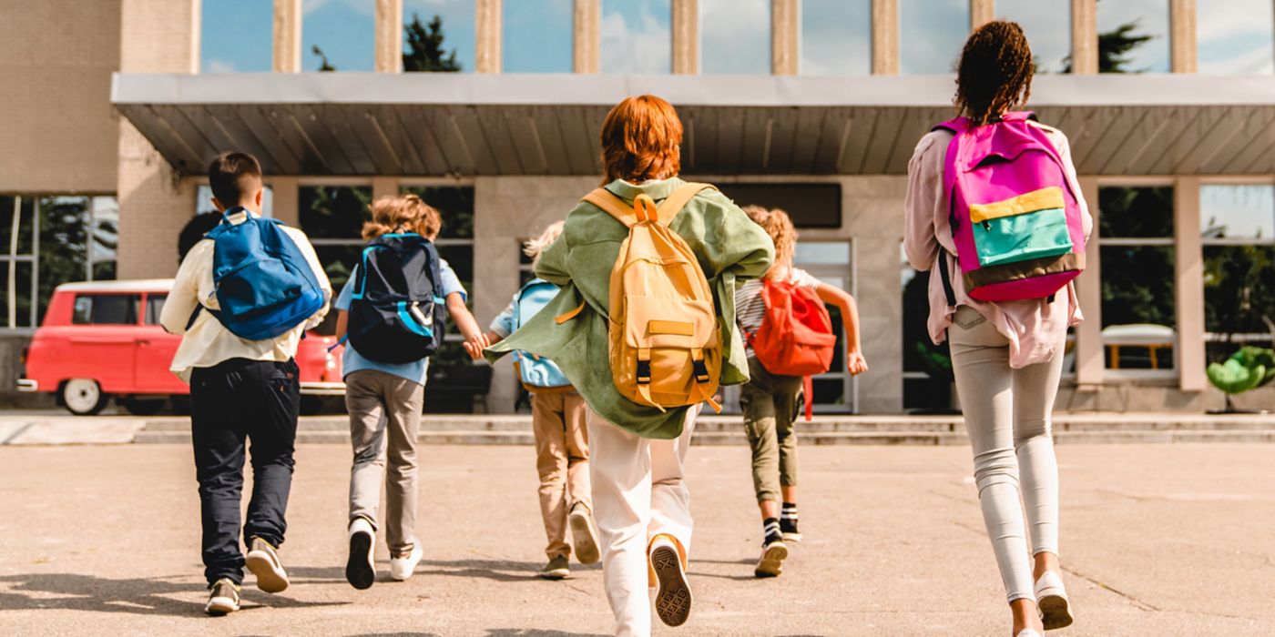 Little kids schoolchildren pupils students running hurrying to the school building for classes lessons from to the school bus. Welcome back to school. The new academic semester year start