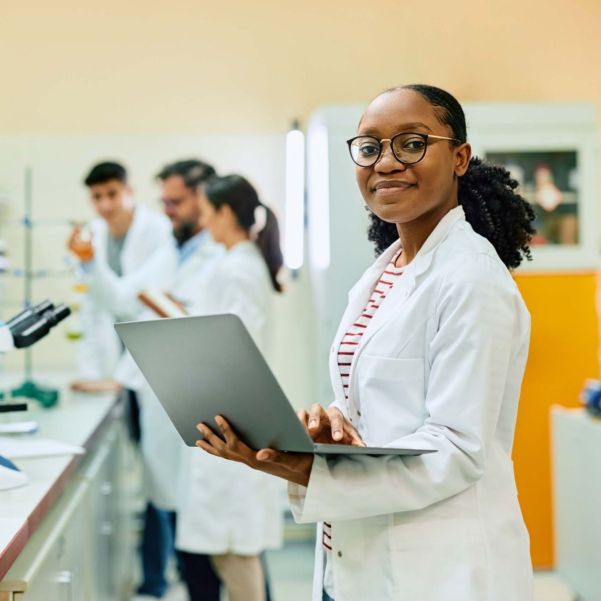 Happy black female chemist working on laptop in laboratory and looking at camera.