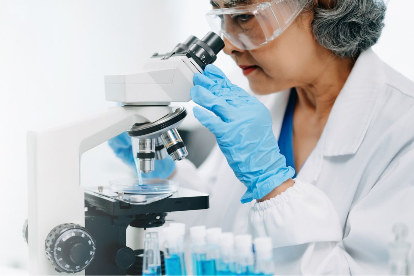 Scientists conducting research investigations in a medical laboratory, a researcher in the foreground is using a microscope in laboratory for medicine.