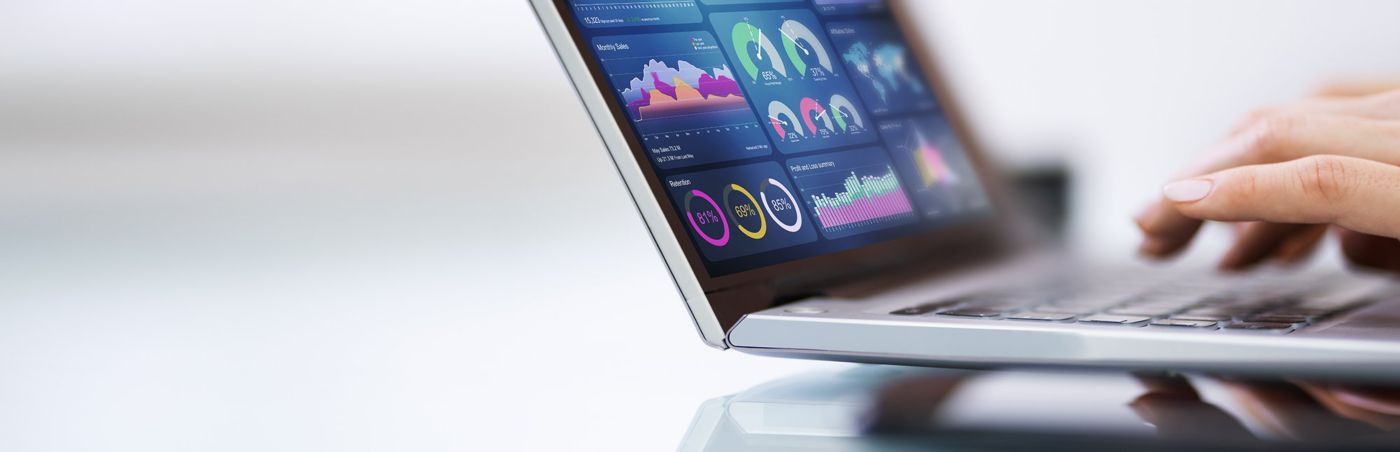 A laptop screen displays colorful operational charts, gauges and analytics dashboards.