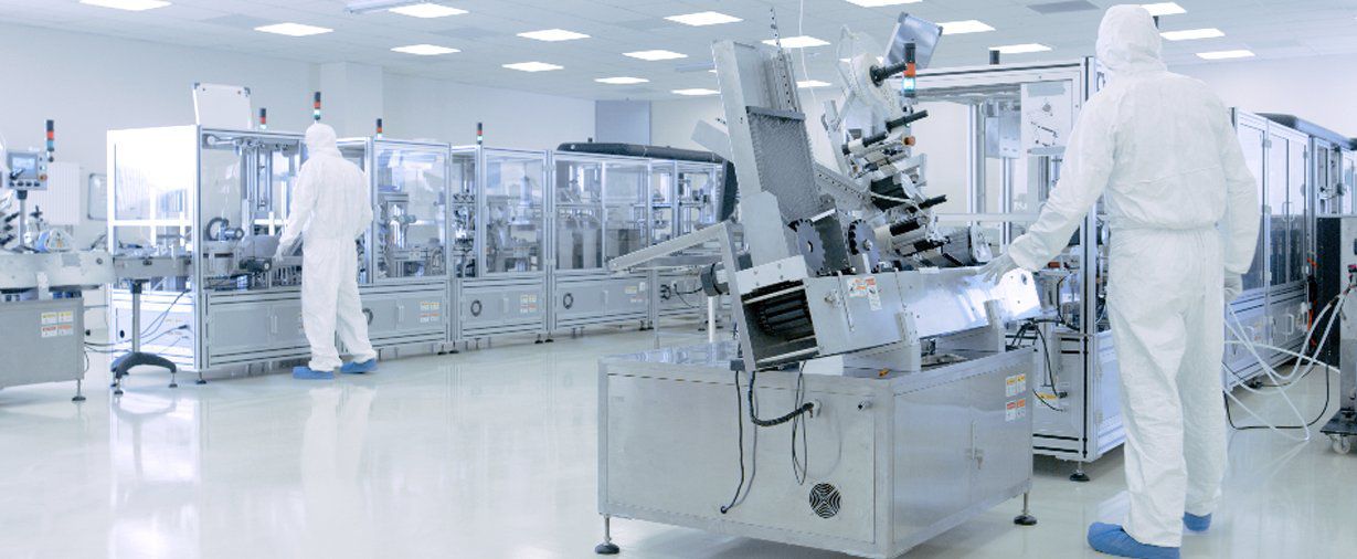 Workers in white protective suits oversee an automated production line inside a cleanroom.