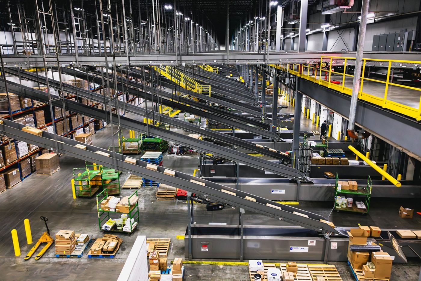 A high-angle view of a modern industrial distribution center featuring complex overhead conveyor belts and organized pallet logistics.