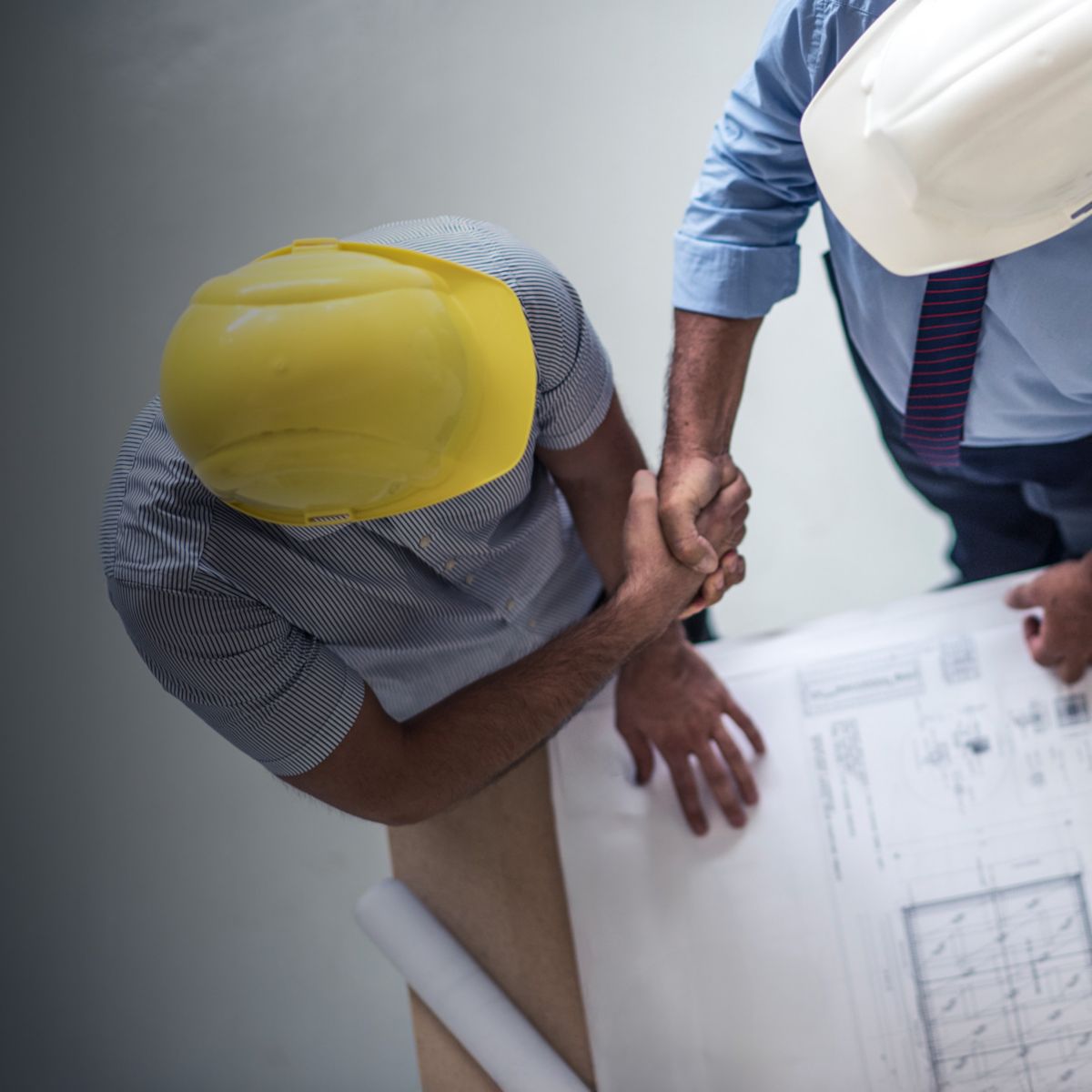 A team of construction professionals wearing hard hats collaborates over blueprints and a laptop. This image highlights teamwork, planning, and project coordination in the construction and engineering industry.