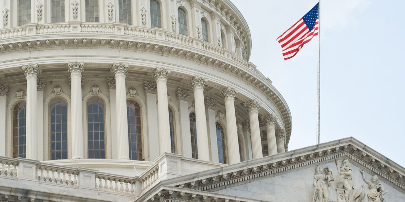 American flag waves beside dome of historic Capitol building.