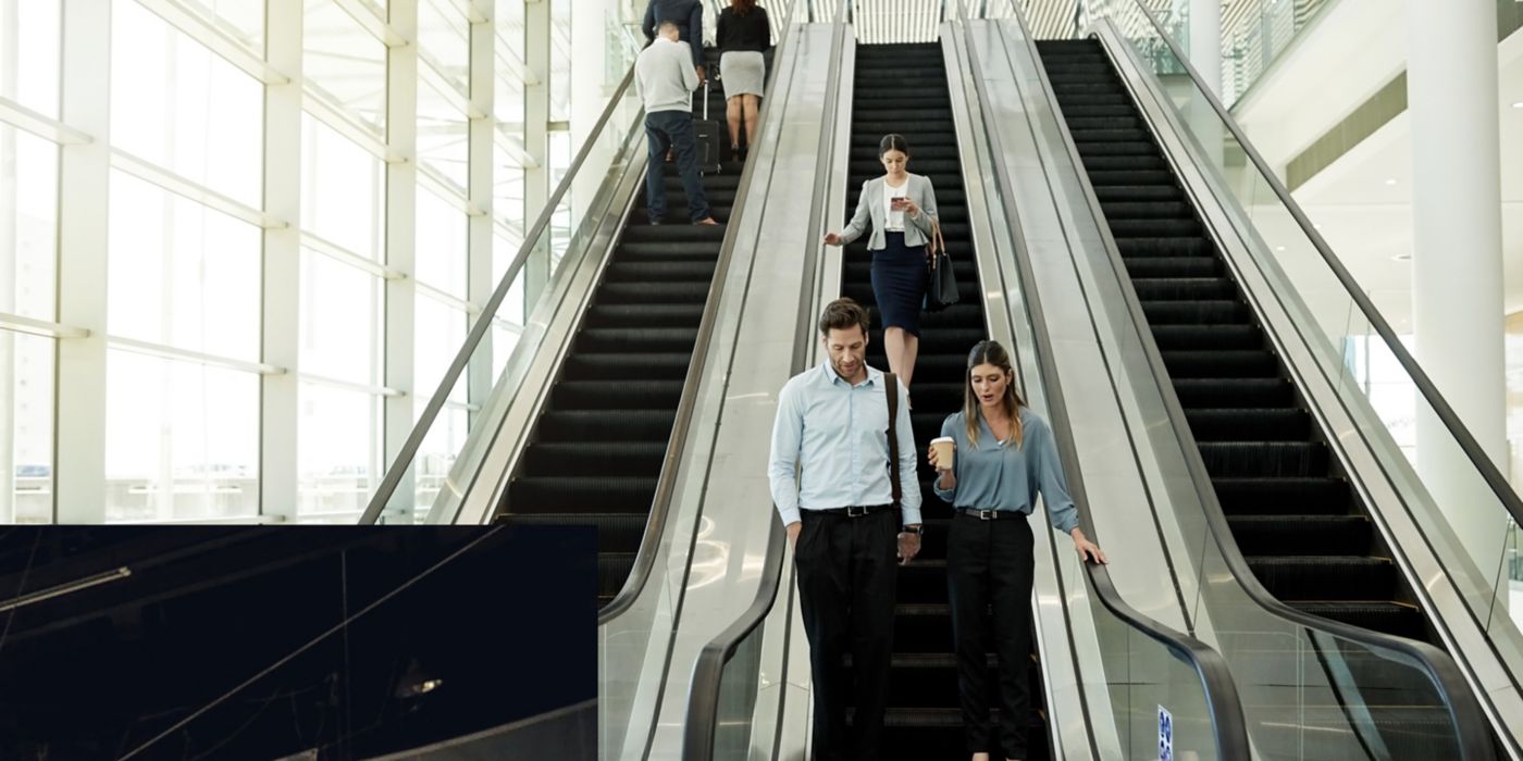 People ride escalators inside bright, modern building with windows.