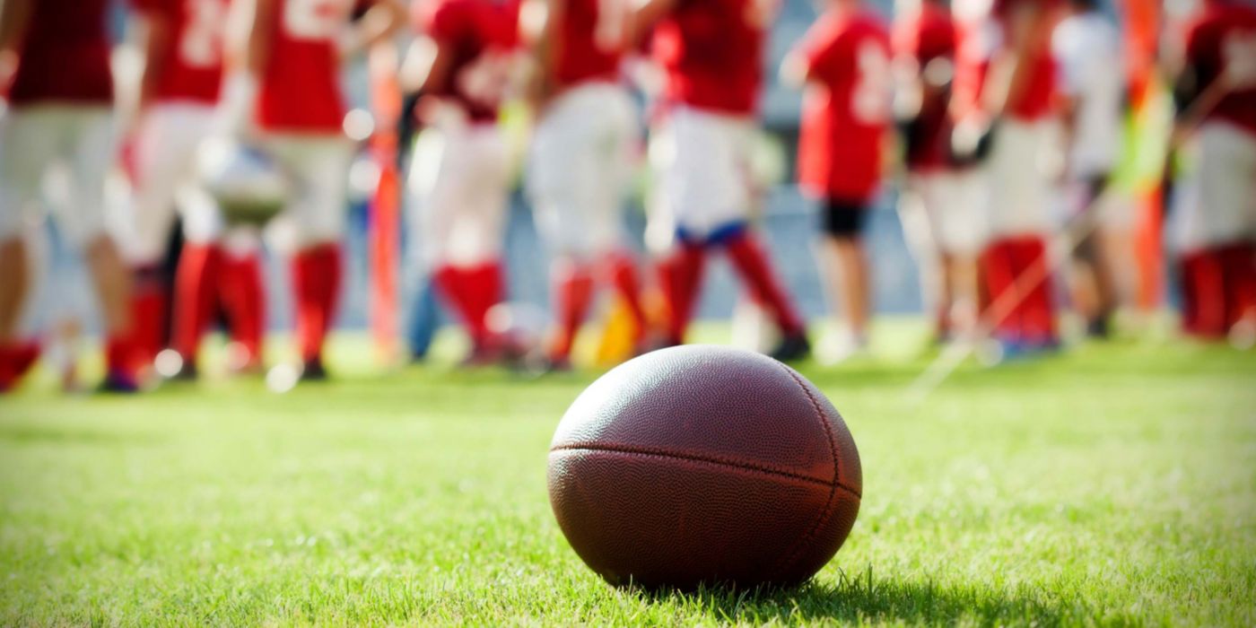Football on grass, players blurred in red uniforms behind.